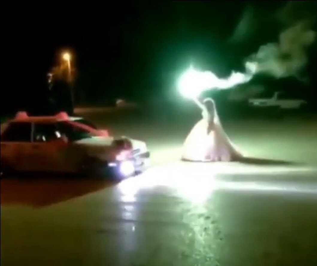 The bride holding light the power of the sun in her hands, facing a wedding car.