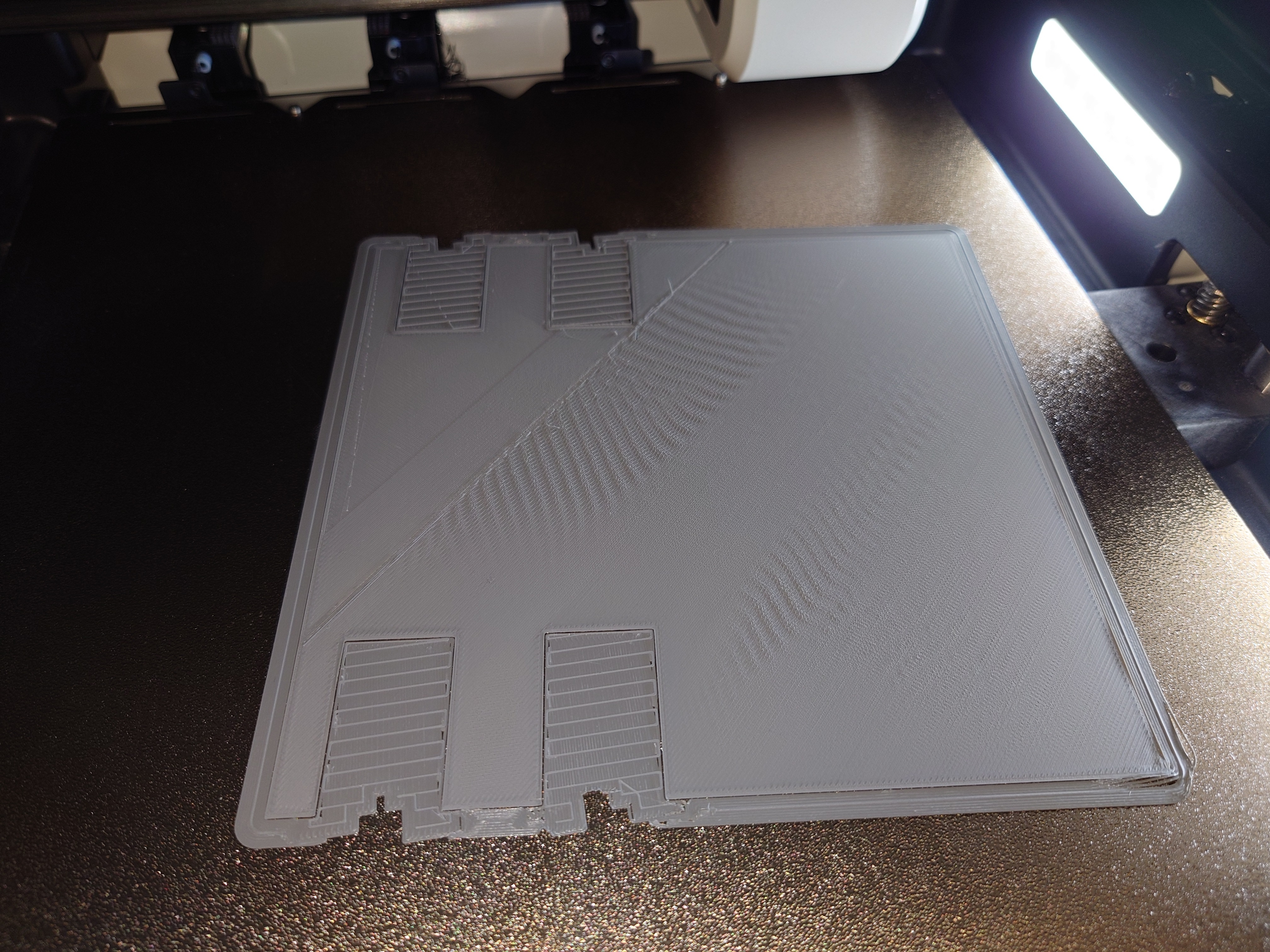 A photo of a 3d printer plate with a partially finished square print on it. the middle of the print has very pronounced wrinkling on the flat layer.