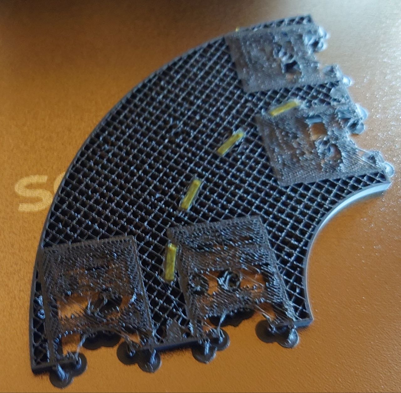 A photo of a half-finished 3D print of a little snap-together road piece on the printer bed. the square infill pattern is full of bumps and scrapes. also the bridges have failed.